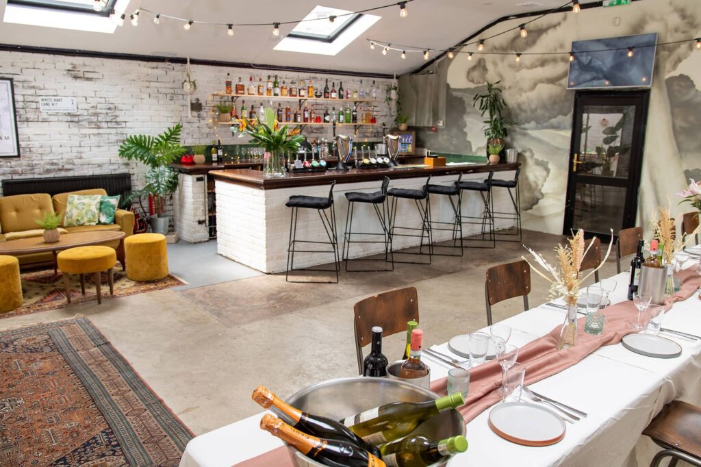 A chic venue with a bar and stools, a lounge area and a long, decorated table for a social event.