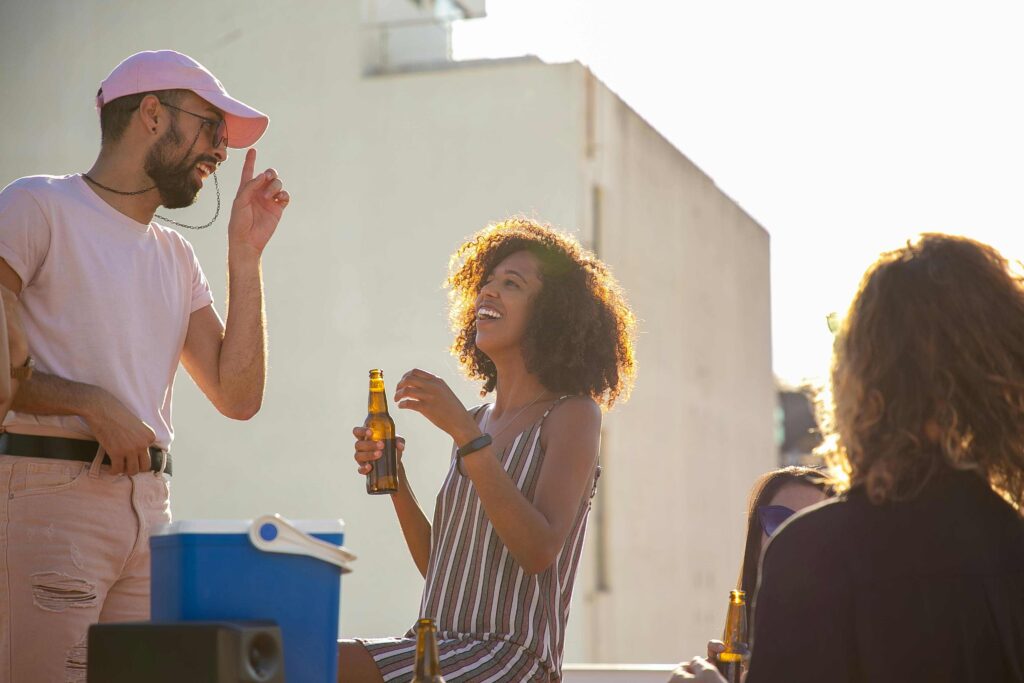 A man and a woman are having a conversation on a sunny rooftop over a beer.