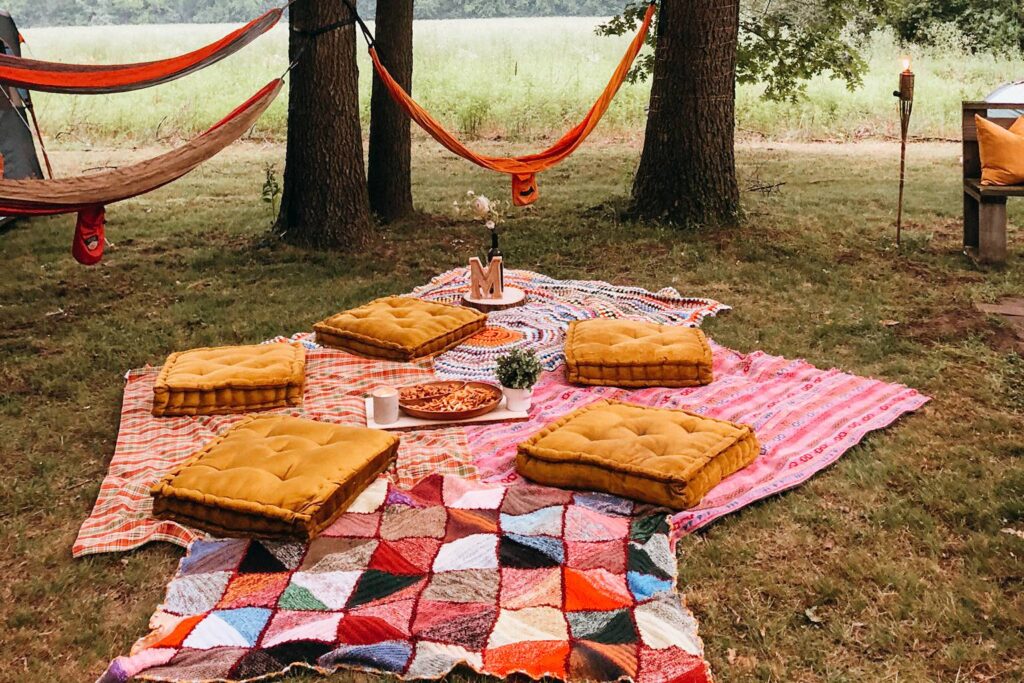 An outdoor picnic setting with cushions, pizza, and hammocks tied to tries in the background