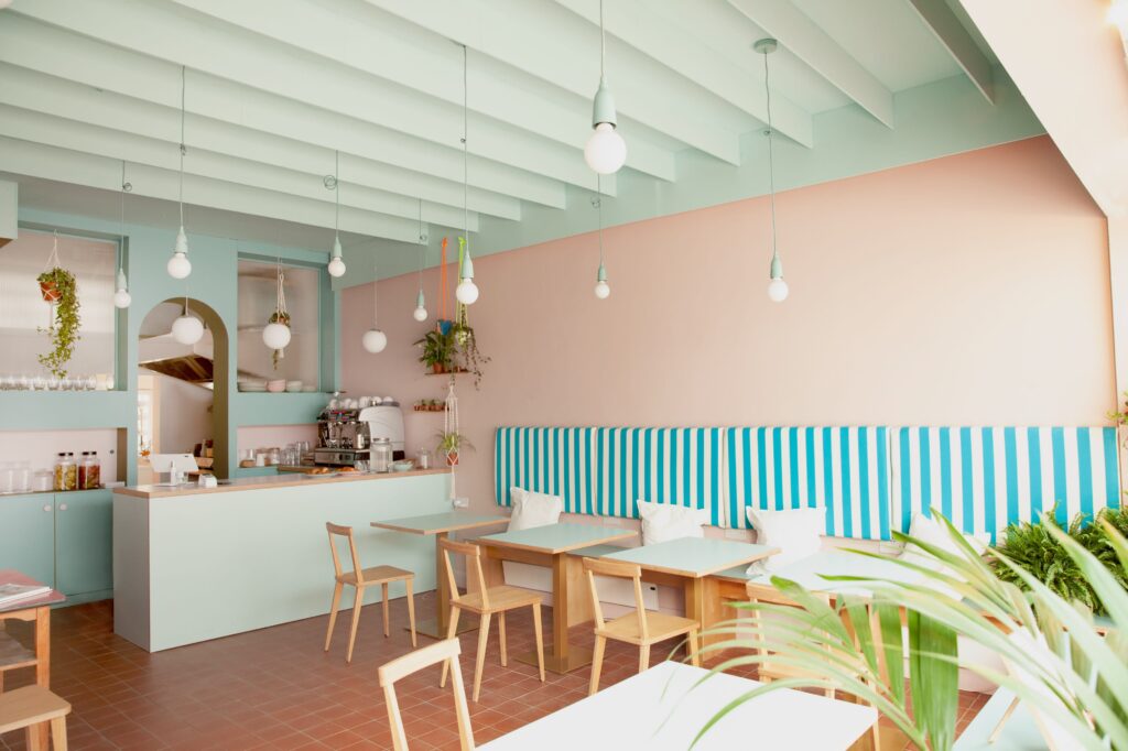 Pastel London cafe interior with mint and peach walls, blue and white striped banquette and hanging plants in macramé holders