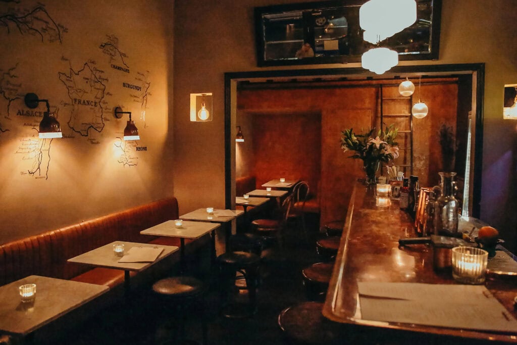 Warmly lit private cocktail bar with leather banquettes and a copper counter in London