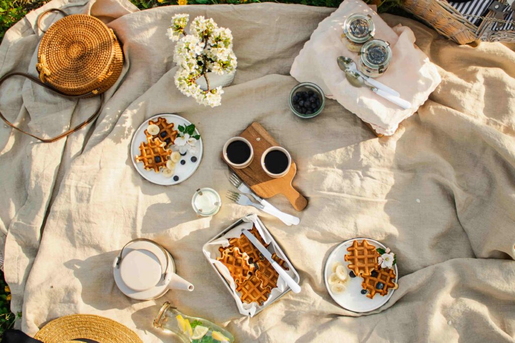 A picnic blanket set with waffle plates, tea, and fruit.