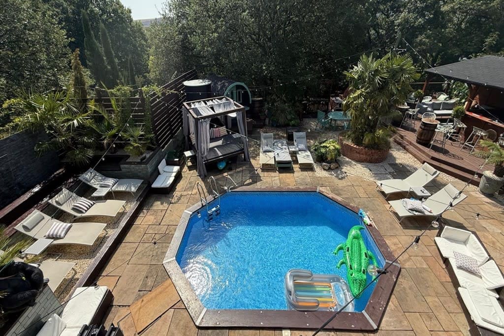 Aerial view of an octagonal private pool with inflatables and sun loungers in a landscaped urban garden, bookable for group hire