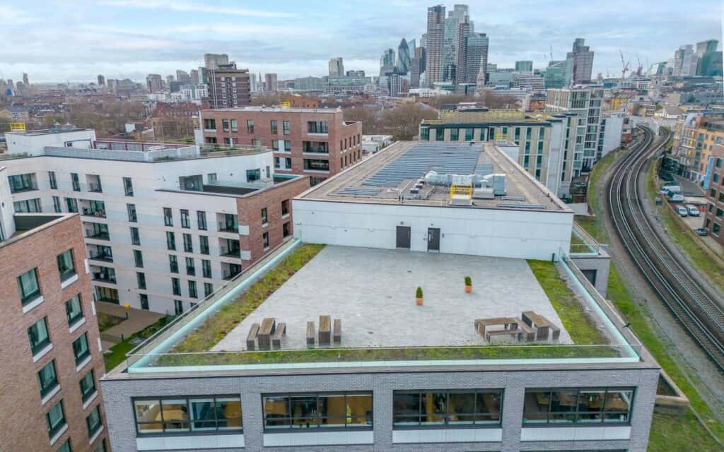 Spacious rooftop rental in Shoreditch with benches, potted plants, and city views overlooking London’s skyline and railway.