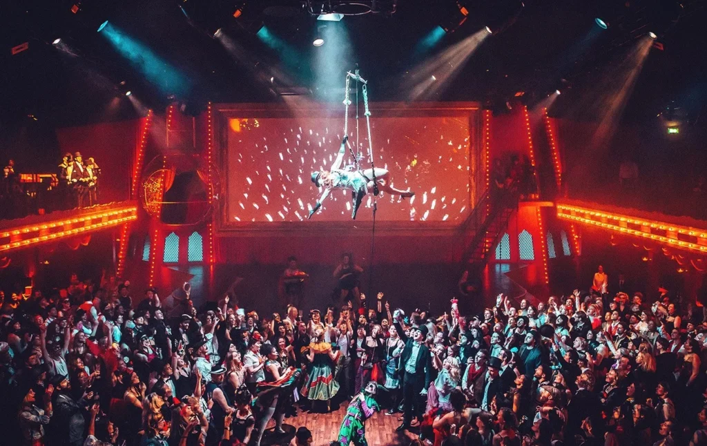 Secret Cinema London immersive production with aerial silk performer above costumed audience in red carnival theatre