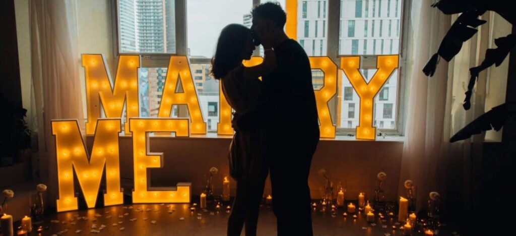 silhouette of a couple standing in front of a marry me sign