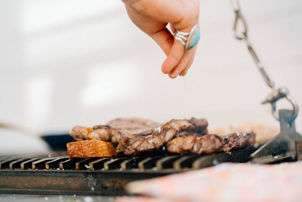A hand salting meat on a grill