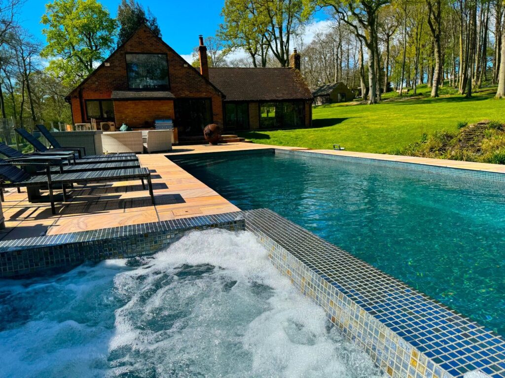 Private outdoor swimming pool and jacuzzi with sun loungers and wooden decking at a country property available to hire by the hour