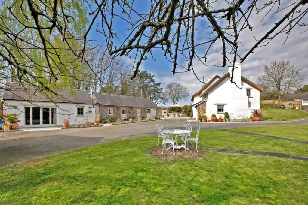 View of an extensive green garden and courtyard with a thatched cottage and two other houses in the background