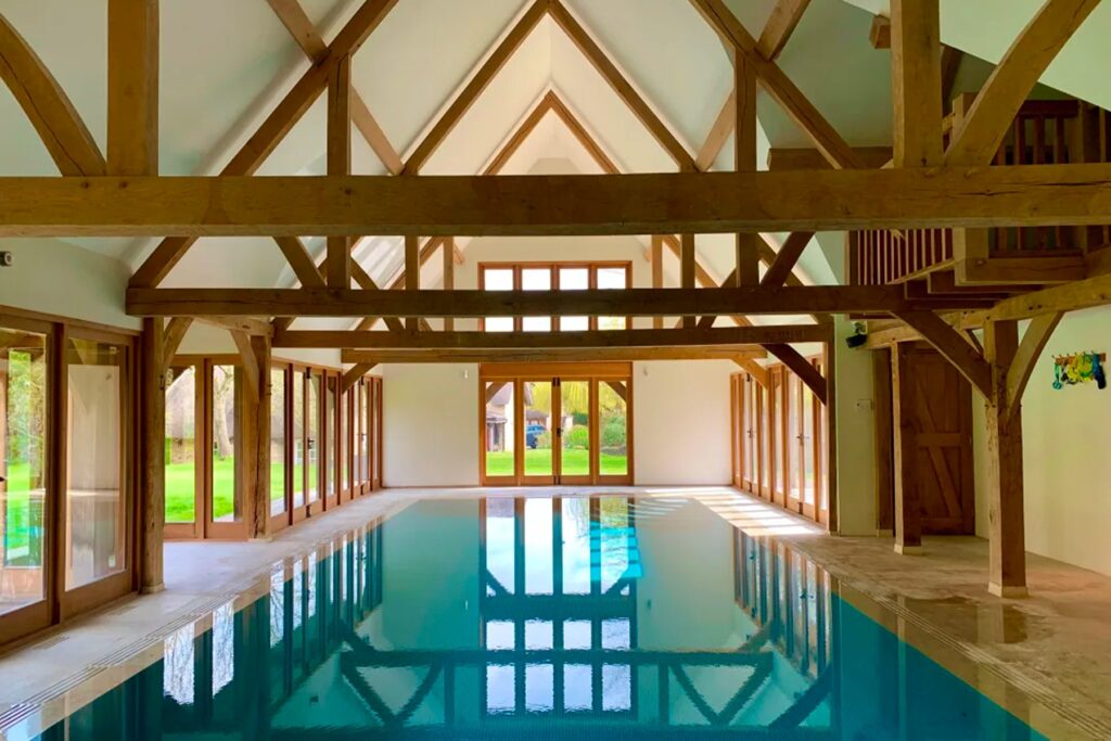 The interior of a thatched cottage in Oxfordshire with a large indoor pool and exposed wooden beams.