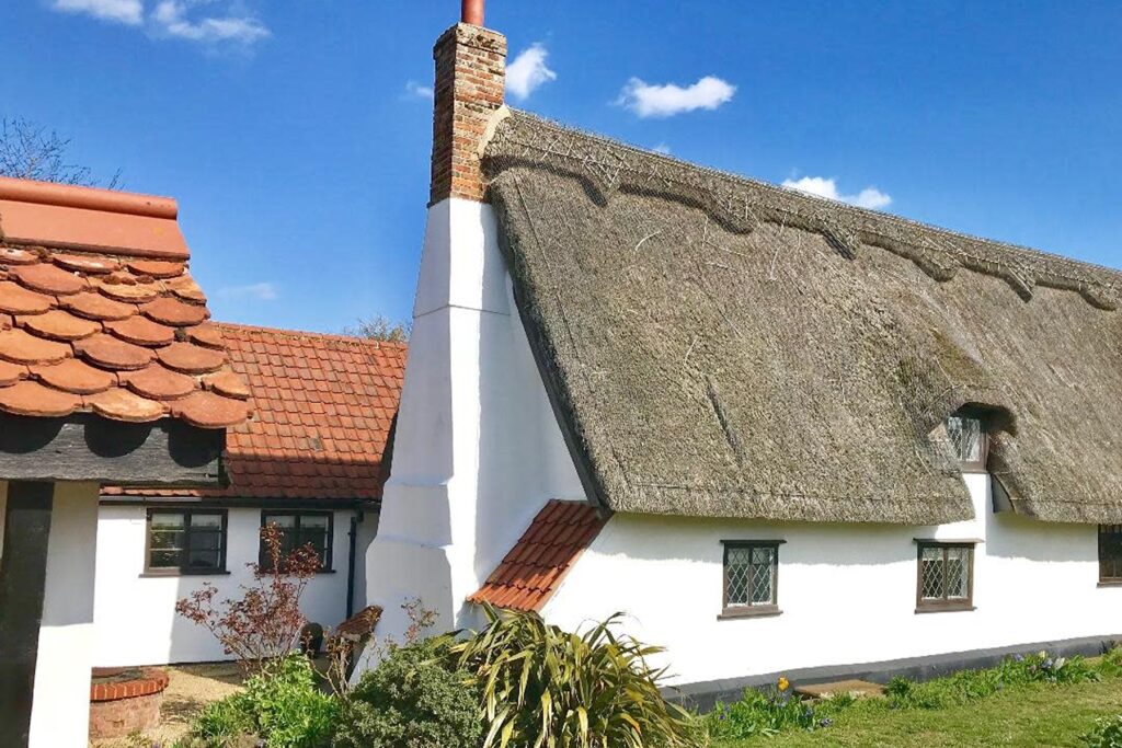 Side view of white thatched cottage and neighboring houses in Suffolk.