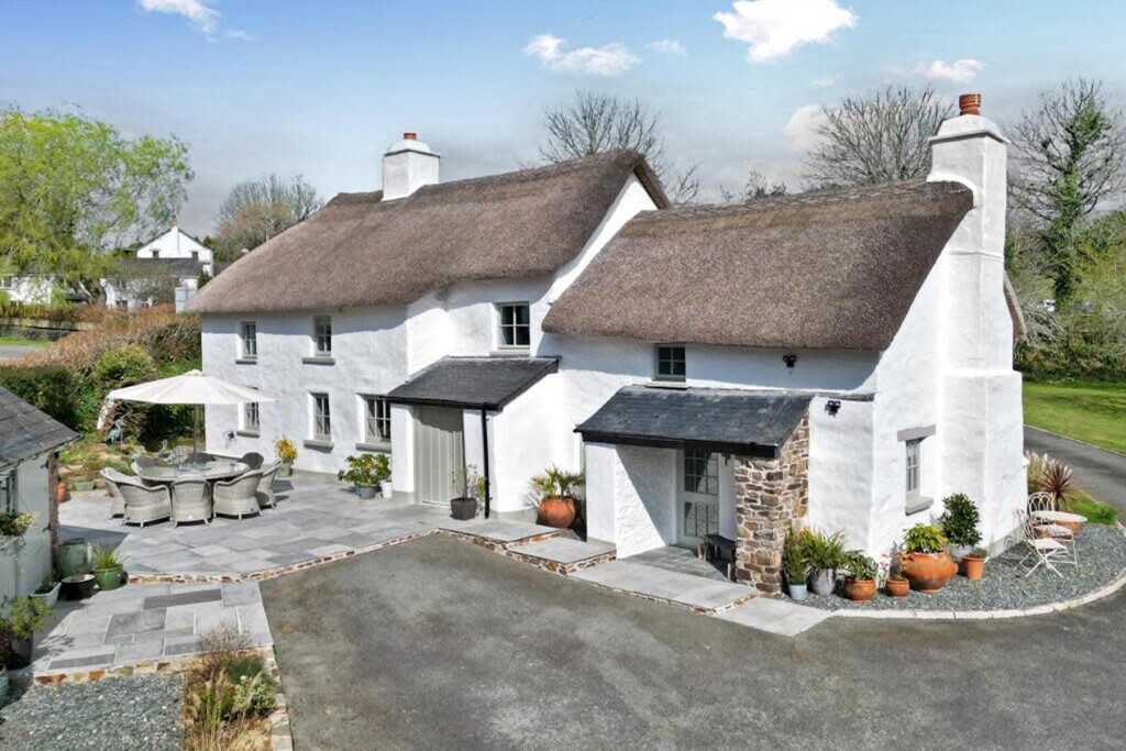 White thatched cottage with chimneys and a small courtyard terrace in the UK.