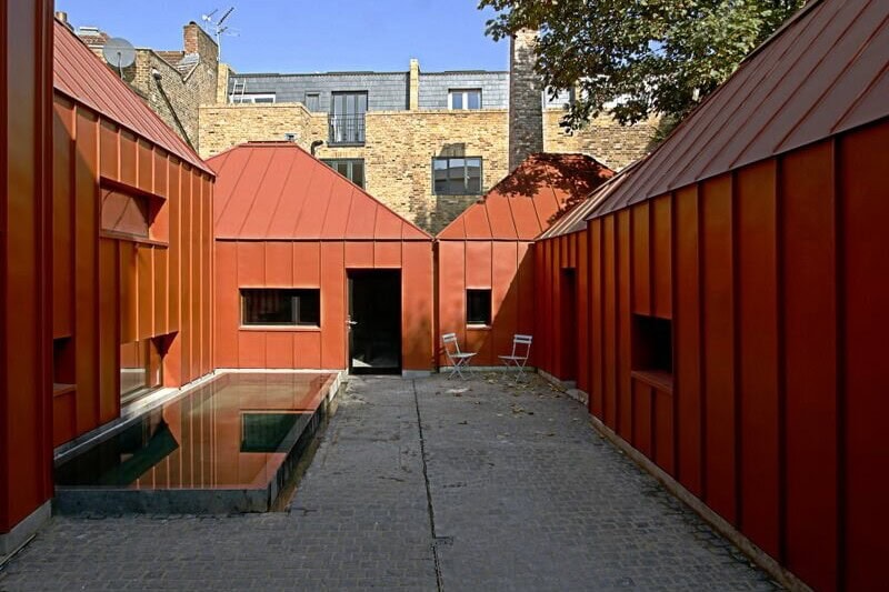 Rust-red metal-clad pavilions surrounding the courtyard of Tin House in Shepherd's Bush.