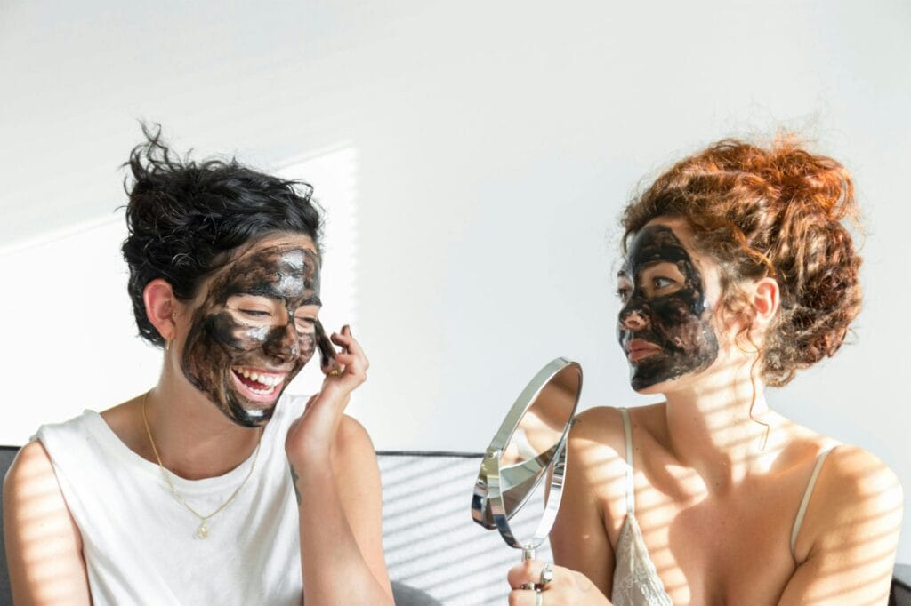 Two women applying black face masks with a hand mirror.