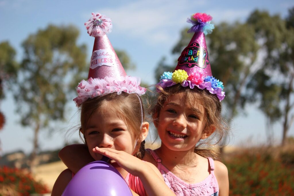 Two girls in an outdoor setting with a balloon and party hats.