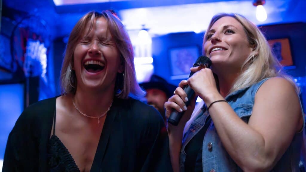 Two women singing karaoke in a dimly lit bar.
