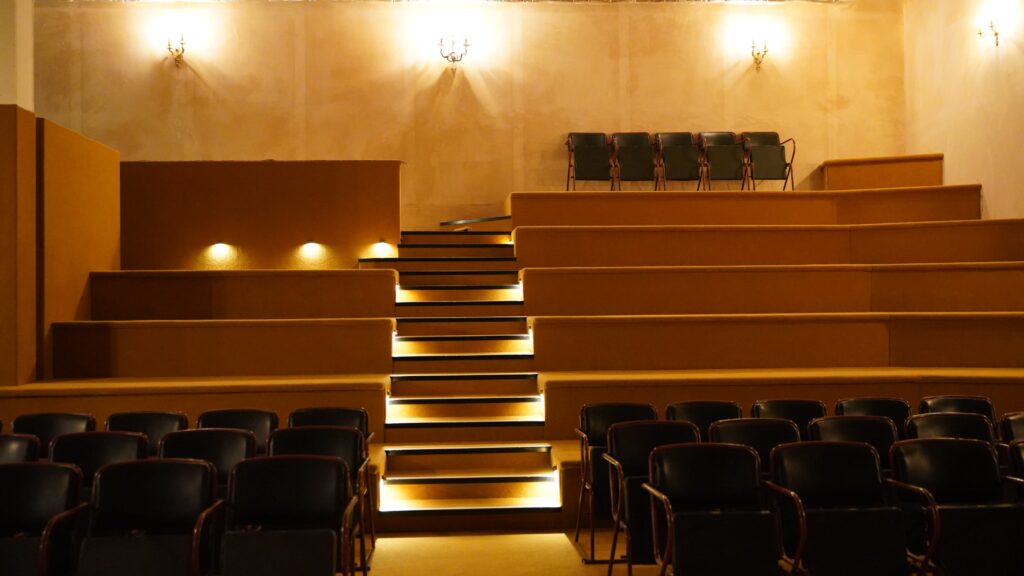 Intimate vintage auditorium with warm lighting, tiered wooden risers and black leather seating, available for theatre hire on Peerspace