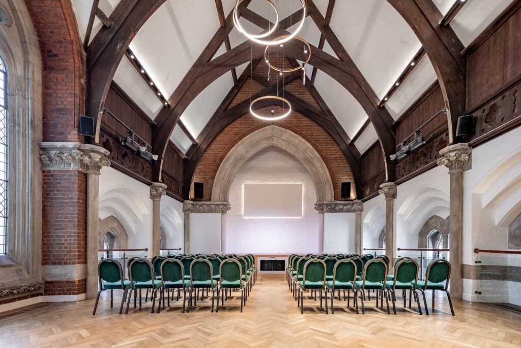 Victorian hall converted church with vaulted ceilings, wooden beams, exposed brick walls, and elegant green chairs