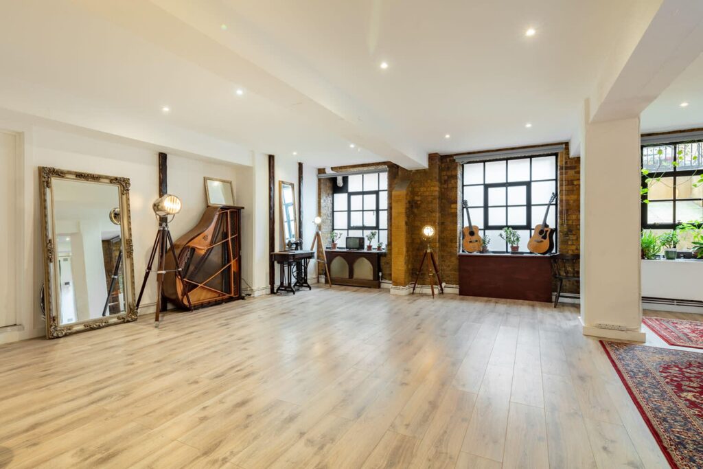 Large warehouse space in London with wooden floors and diverse props, from piano to lighting, a mirror and guitars.
