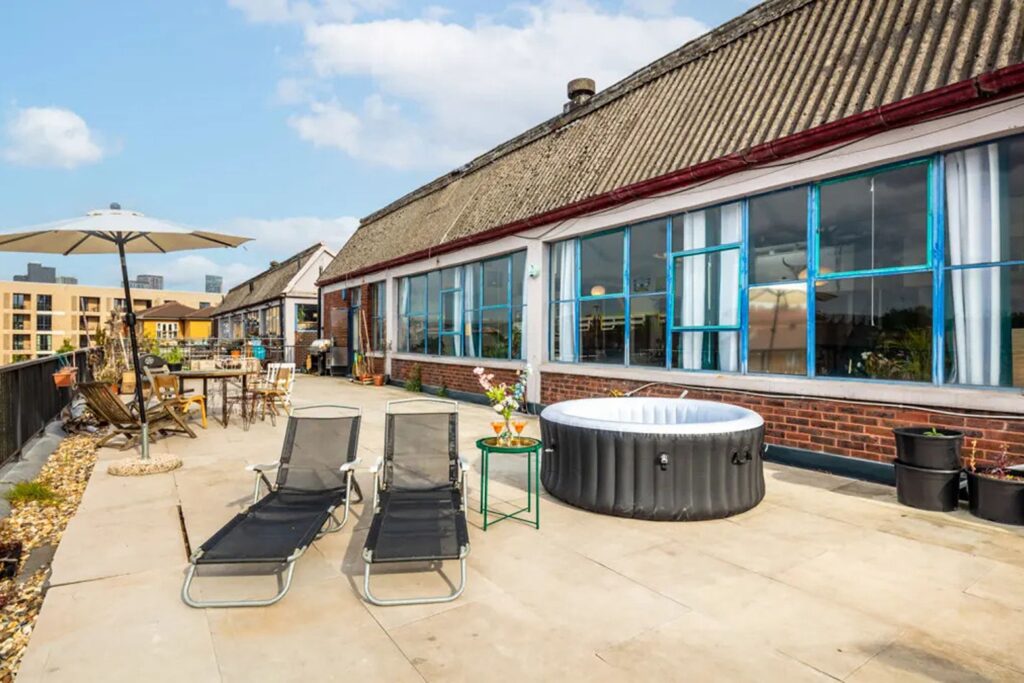 Rooftop terrace of a warehouse in London on a sunny day, with lounge chairs, an inflatable pool and sun umbrellas.