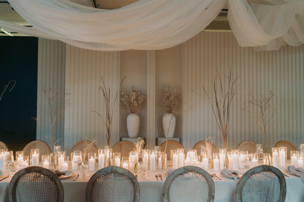 Elegant wedding reception venue dinner setup with candles, neutral decor, and draped fabric ceiling above the table.