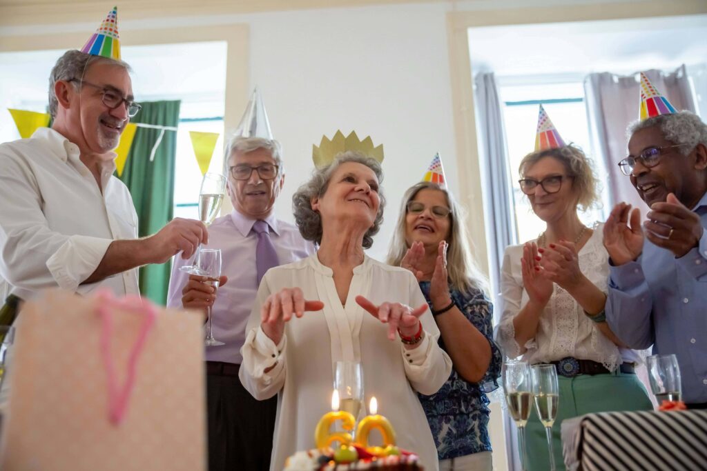 A woman celebrating her 60th birthday with cake and a group of friends, wearing party hats.