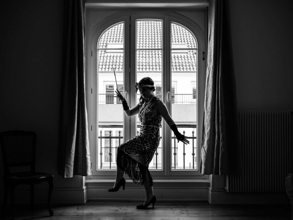 Woman in 1920's attire posing in front of a window.