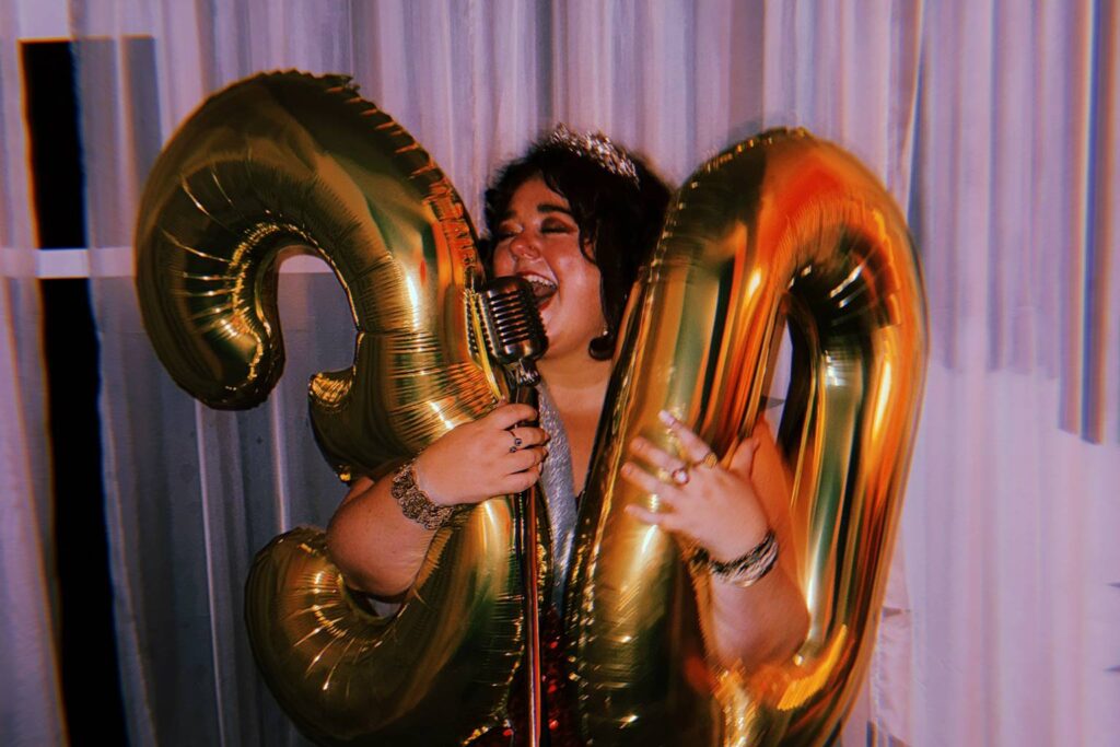 A woman with 30th birthday balloons singing into a microphone.