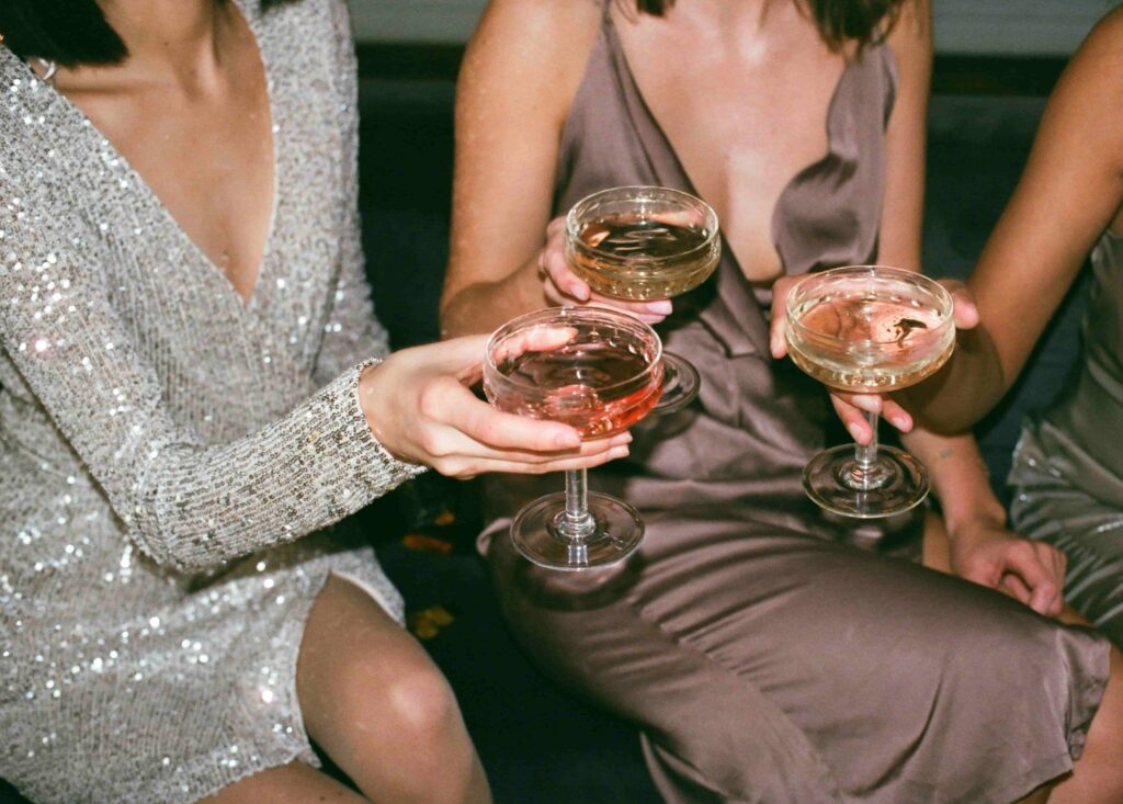 Three women in elegant dresses toasting with fancy cocktail glasses.