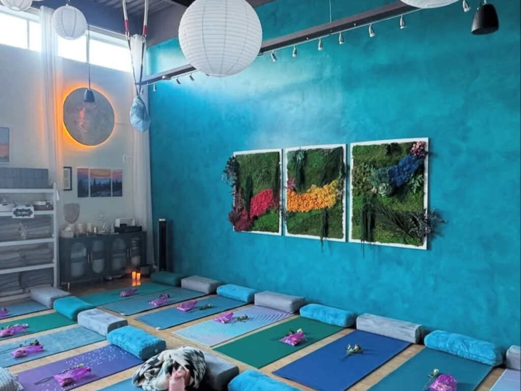 A well-lit yoga studio space with floor mats and blue walls decorated with art.