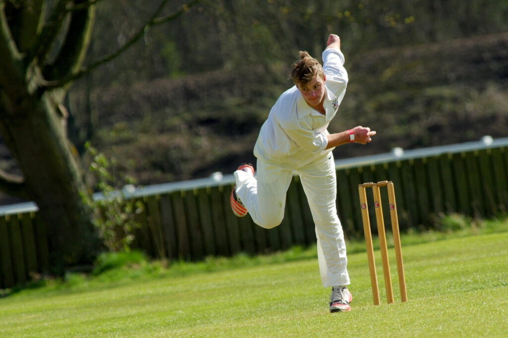 A young man playing cricket on a grass field.